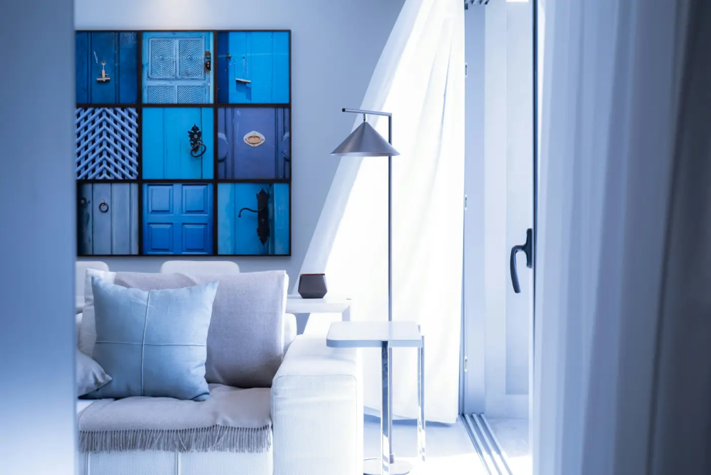 Modern living room with a blue-themed artwork of doors, a light-colored sofa with blue pillows, and a silver floor lamp.