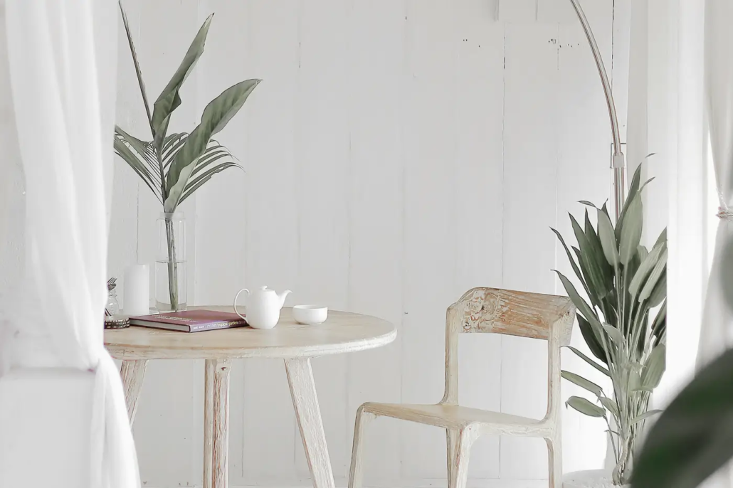 Bright white dining space featuring a light wooden chair, a book on a table, and decorative plants.