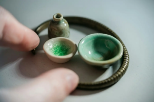 Miniature ceramic bowls and vase with green glaze next to fingers for scale