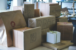Collection of personalized kraft paper gift boxes with handwritten names including John, Christopher, Julie, and Manuel, tied with twine and ribbon.