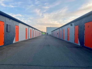 Row of drive up storage units with bright orange doors at Pacific Rim Storage Victoria, showing wide lanes and easy vehicle access.