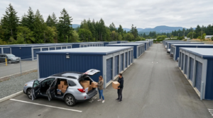 A man and woman unloading cardboard boxes from a silver SUV at an outdoor self-storage facility in Victoria, BC.